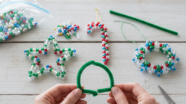 Finished beaded Christmas ornaments, including a star, a candy cane, and a small wreath, along with loose colorful beads.