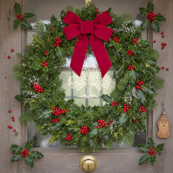Christmas wreath of holly with red berries and a large red bow on a wooden door.