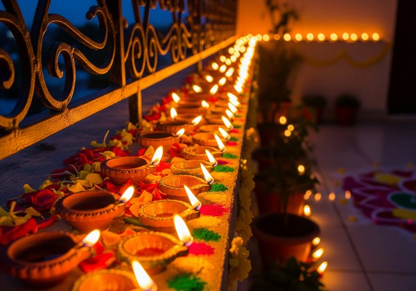 A balcony railing lined with lit clay diyas, creating a warm border of light