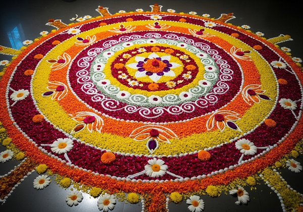 A colorful rangoli design made entirely from fresh flower petals, including marigolds, roses, and other blossoms