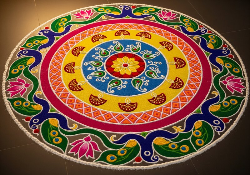 A rangoli design composed of concentric circles, filled with different colored powders